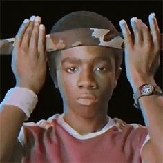 a young man wearing a baseball cap and holding his hands up to his head while looking at the camera