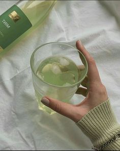 a hand holding a glass filled with ice and water next to a bottle of wine