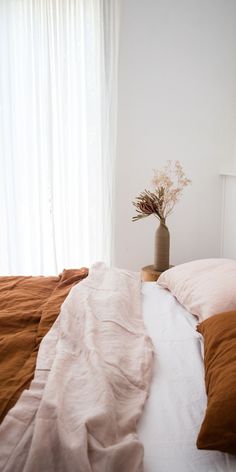 an unmade bed with two pillows and a plant in the corner next to it