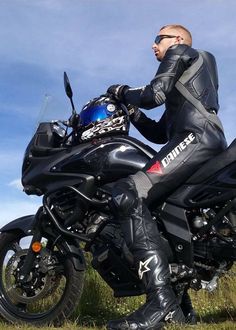 a man in black leather riding on the back of a motorbike with blue sky and clouds behind him