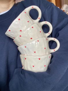 three white cups with red hearts on them are stacked in the middle of a woman's lap