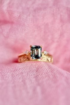 an engagement ring on top of a pink cloth with a green stone in the center