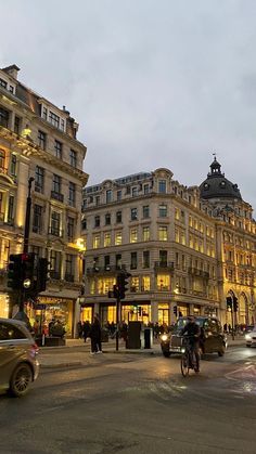 a busy city street at dusk with cars and people crossing the street in front of buildings