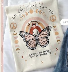 a white t - shirt with a pink butterfly and peace sign on it, next to a pair of jeans