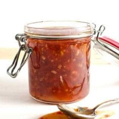 a glass jar filled with red sauce sitting on top of a table next to a spoon