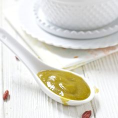 a spoon full of green sauce sitting on top of a white plate next to a cup