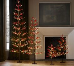 two christmas trees with lights in front of a fireplace