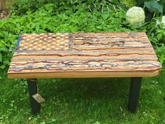 an american flag made out of wood sitting on top of green grass in front of bushes