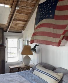 an american flag hanging over a bed in a room with white walls and wood floors