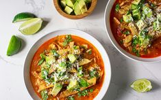 two bowls of soup with tortilla and avocado on the side