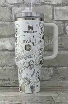 a white travel mug with the words stanley on it sitting against a brick wall in front of a wooden floor