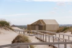 a wooden walkway leading to a building on top of a sandy hill with sand dunes in the background