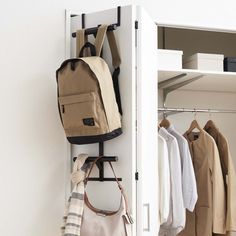 an open closet with clothes and bags hanging on the door handle, in front of a white wall