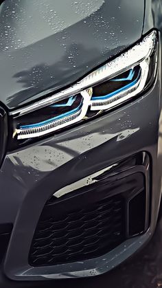 the front end of a grey car with its lights on and rain drops all over it