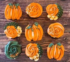 cupcakes decorated with orange frosting and green leaves on top of a wooden table