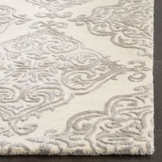 a white rug with an intricate design on it's side, in front of a dark wood floor