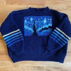 a knitted blue sweater with a tree and stars on the front, sitting on a wooden floor