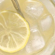 a lemon slice is sitting on top of ice in a glass with water and silver spoon