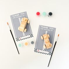 two small wooden toy cars sitting on top of each other next to paint and brushes