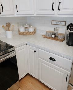 a kitchen with white cabinets and stainless steel stove top oven, dishwasher and coffee maker