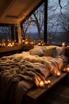 a bed covered in blankets and candles next to a window with lights on the windowsill