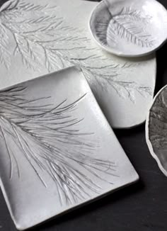 three white dishes sitting on top of a black table next to plates and spoons