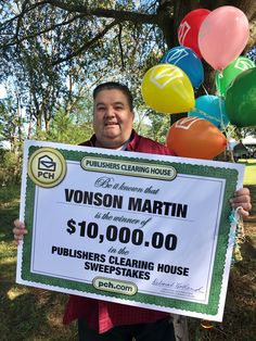 a man holding up a large check for $ 10, 000 in front of balloons