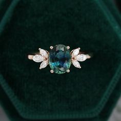 an emerald colored ring with two white diamonds on it in a green velvet jewelry box