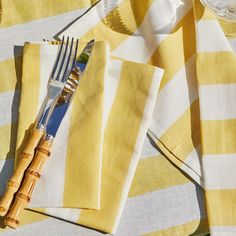 yellow and white striped table cloth with silverware on it, next to wine glass