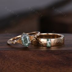 two gold wedding rings with green and white stones on top of each other sitting on a wooden table