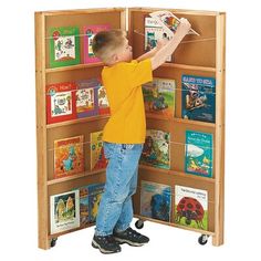 a young boy standing in front of a bookshelf filled with children's books