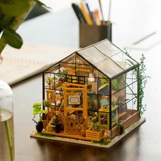 a miniature house made out of wood and glass on top of a table next to a potted plant