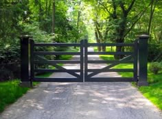 an open gate in the middle of a dirt road with grass and trees around it