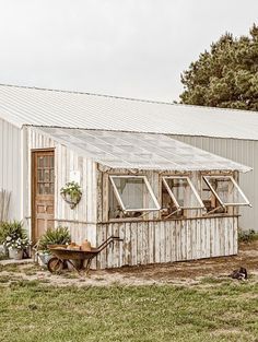 an old white building with windows and a wheelbarrow in the grass next to it