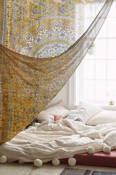 an unmade bed with blankets and pom - poms on the floor in front of a window