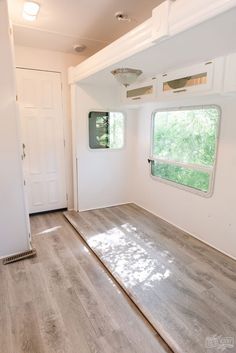 an empty room with wood flooring and white walls in the background is a door leading to a window