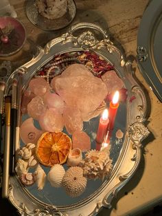 an assortment of seashells and candles on a silver platter with other items