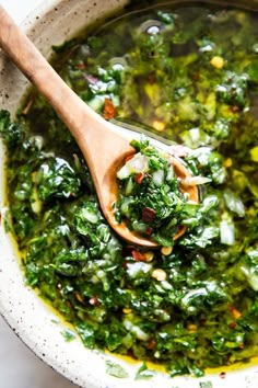 a wooden spoon is in a bowl filled with greens and other vegetables that are mixed together