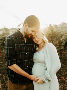 a pregnant couple cuddles in an apple orchard at sunset during their family's photo session