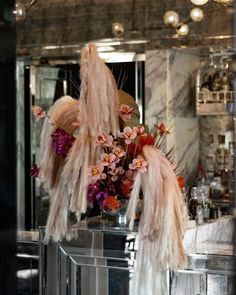 flowers and feathers are displayed in front of a mirror at a bar with liquor bottles on the counter