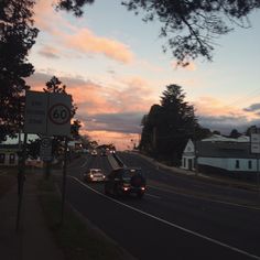 a car is driving down the road at sunset or dawn with clouds in the sky