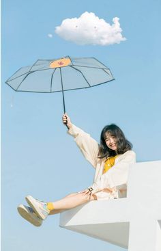 a woman sitting on top of a white wall holding an umbrella over her head while flying through the air