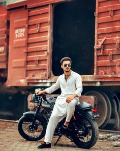 a man sitting on top of a motorcycle next to a train car with cargo containers in the background