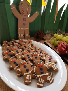 a white plate topped with lots of cut out gingerbreads next to a table full of grapes