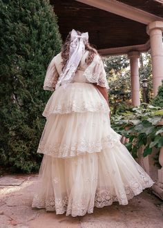 a woman in a white dress is standing near some bushes and trees with her back to the camera