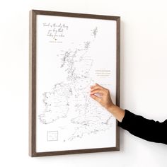 a person is writing on a map in front of a white wall with a brown frame