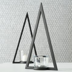 two triangle shaped candles are sitting next to each other on a table in front of a wall