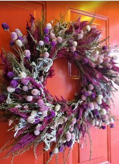 a wreath with purple flowers hanging on a red front door by an orange door frame