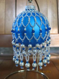 a blue ornament hanging from a hook on a wooden table with beads and pearls