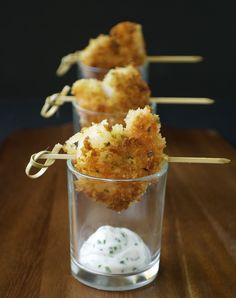 three small cups filled with food on top of a wooden table and toothpicks sticking out of them